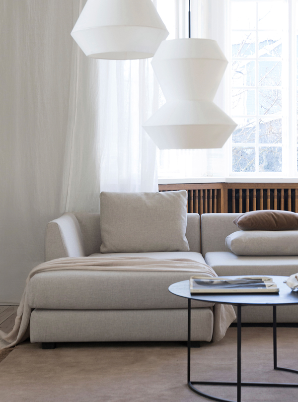 Modern minimalist living room with a light gray sectional Hvile module sofa, featuring a chaise lounge, geometric pendant lights, and sheer white curtains allowing natural light.