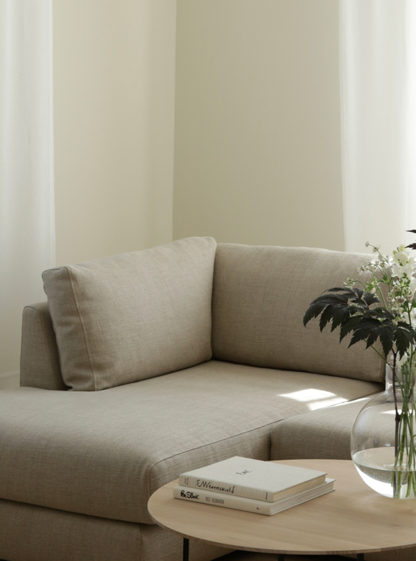 Alt text: "Cozy living room with a beige sectional Hvile module sofa, featuring a round wooden coffee table adorned with books and a bouquet of flowers.