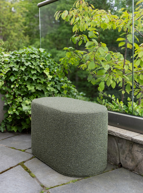 Green Mingle outdoor pouf on a stone patio, next to lush greenery and a glass railing.