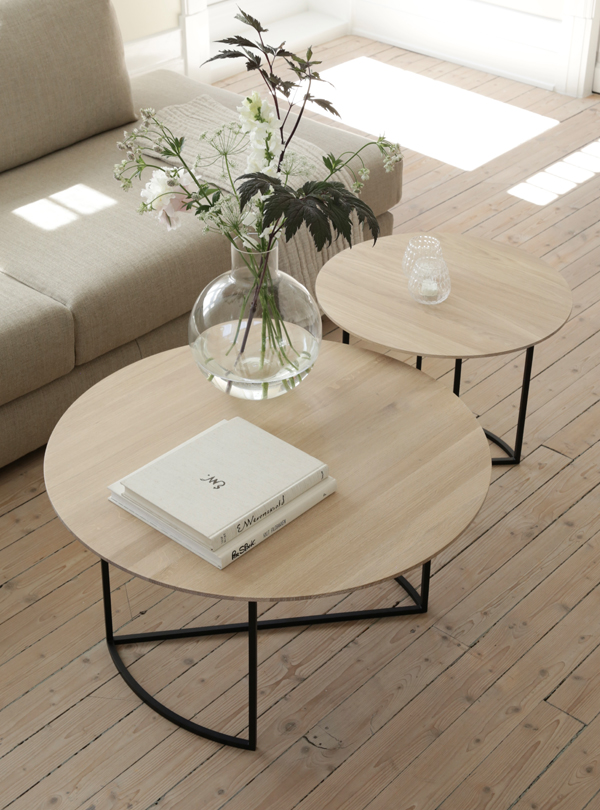 Alt text: "Modern living room with Ljå coffee table set, featuring light wooden tops and black metal legs, complemented by a vase of flowers and books.