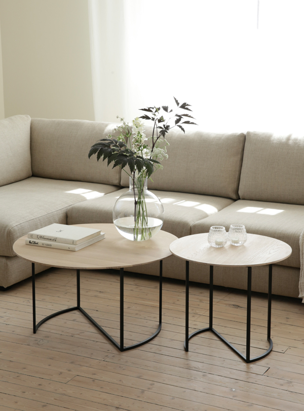Alt text: "Modern living room with Ljå coffee table set, featuring light wooden tops and black metal legs, complemented by a vase of flowers and books.
