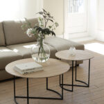 Alt text: "Modern living room with Ljå coffee table set, featuring light wooden tops and black metal legs, complemented by a vase of flowers and books.