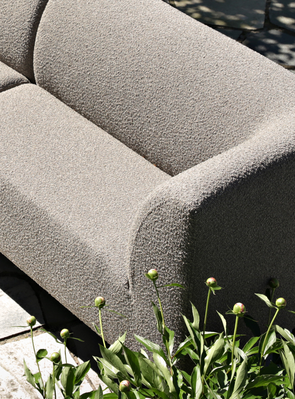 1K_Sofa-Aften-outdoor-62-Pebble-Birch_20 Close-up of the textured, light gray upholstery on an Aften outdoor dining sofa, with green peony buds in the foreground.