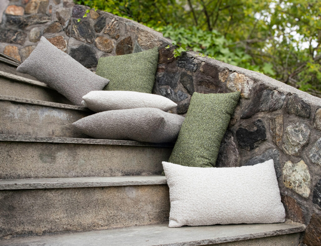 Hynne outdoor cushions in cream, gray, and green, casually arranged on stone steps against a stone wall.