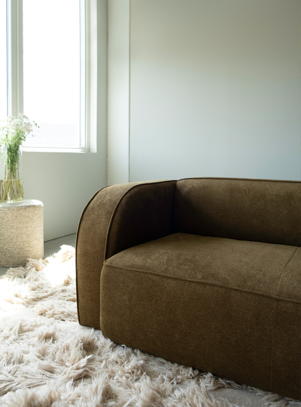 1K_NySofa-Yme_01 Sva module sofa in brown, displayed in a brightly lit room on a plush cream rug.
