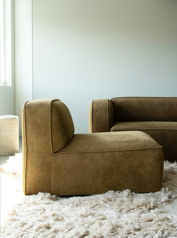 1K_NySofa-Yme_03 Side view of the Sva module sofa in brown upholstery, placed on a cream-colored shaggy rug.