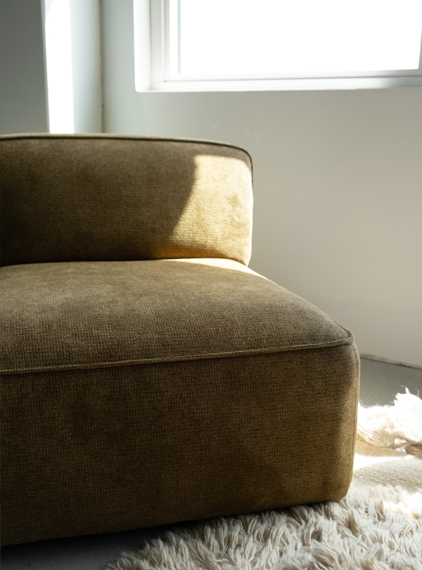 Brown Sva module sofa, partially lit by natural light from a nearby window, placed on a cream-colored shaggy rug.
